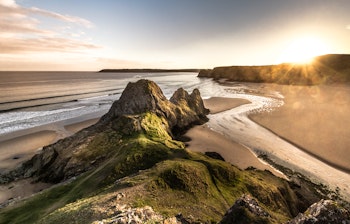 Spektakulær solnedgang over Three Cliffs Bay på Gower-halvøen i Wales med gyldent lys over den smukke kystlinje