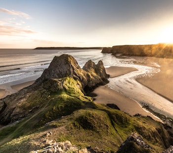 Spektakulær solnedgang over Three Cliffs Bay på Gower-halvøen i Wales med gyldent lys over den smukke kystlinje