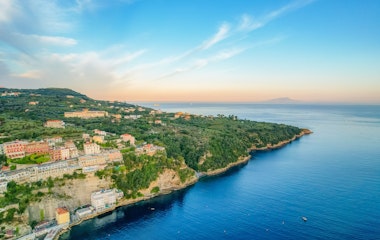 Betagende udsigt over Sorrento by på Amalfikysten ved solopgang, med farverige bygninger på klipperne og det azurblå Middelhav