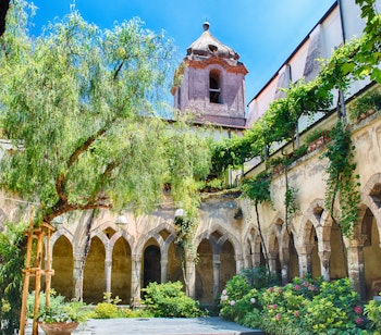 Idyllisk klosterhave i San Francesco d'Assisi kirken i Sorrento med historiske stensøjler og frodig have under blå himmel