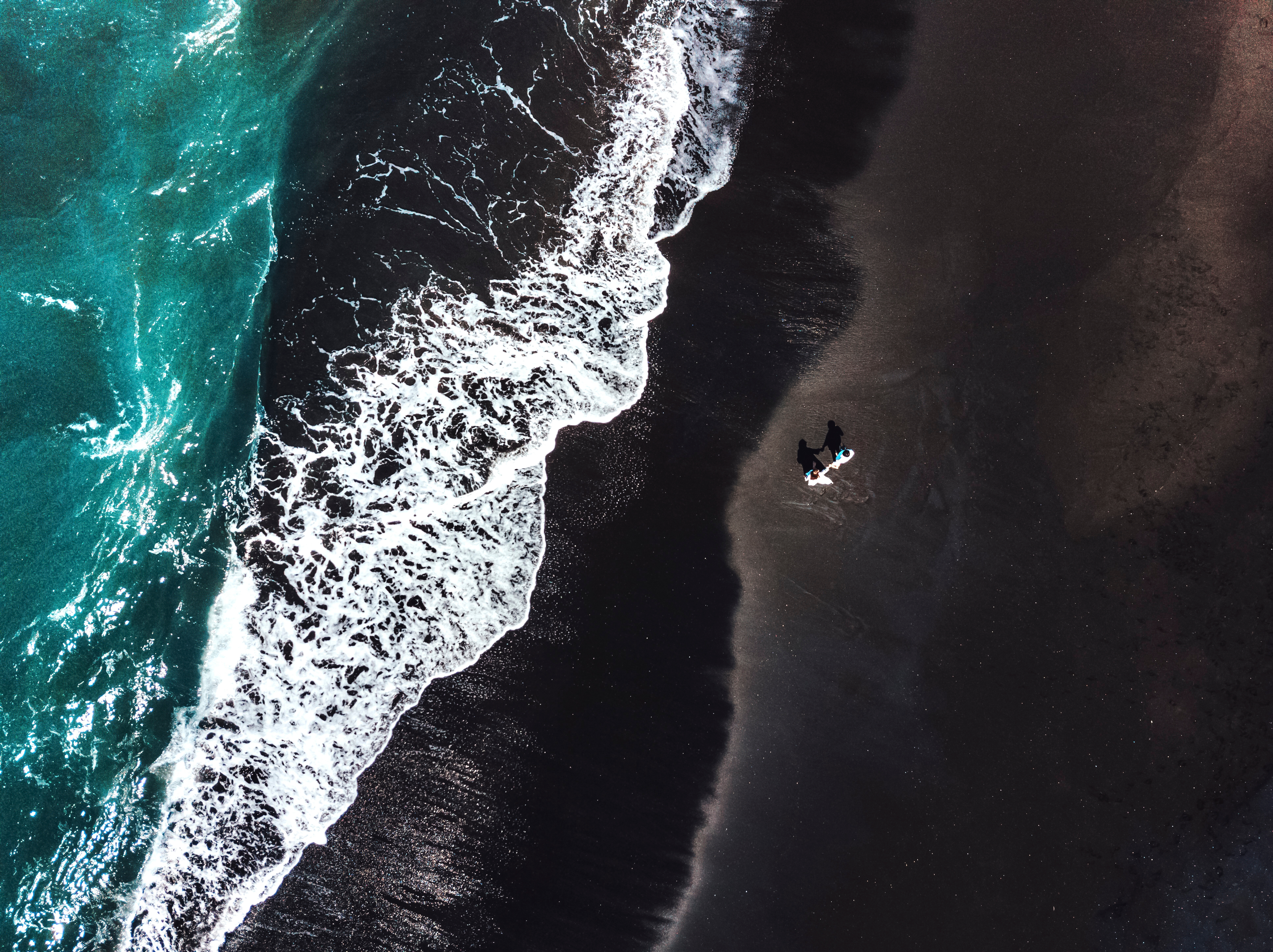 Luftfoto af person på sort vulkansk strand med turkisblå havboelger
