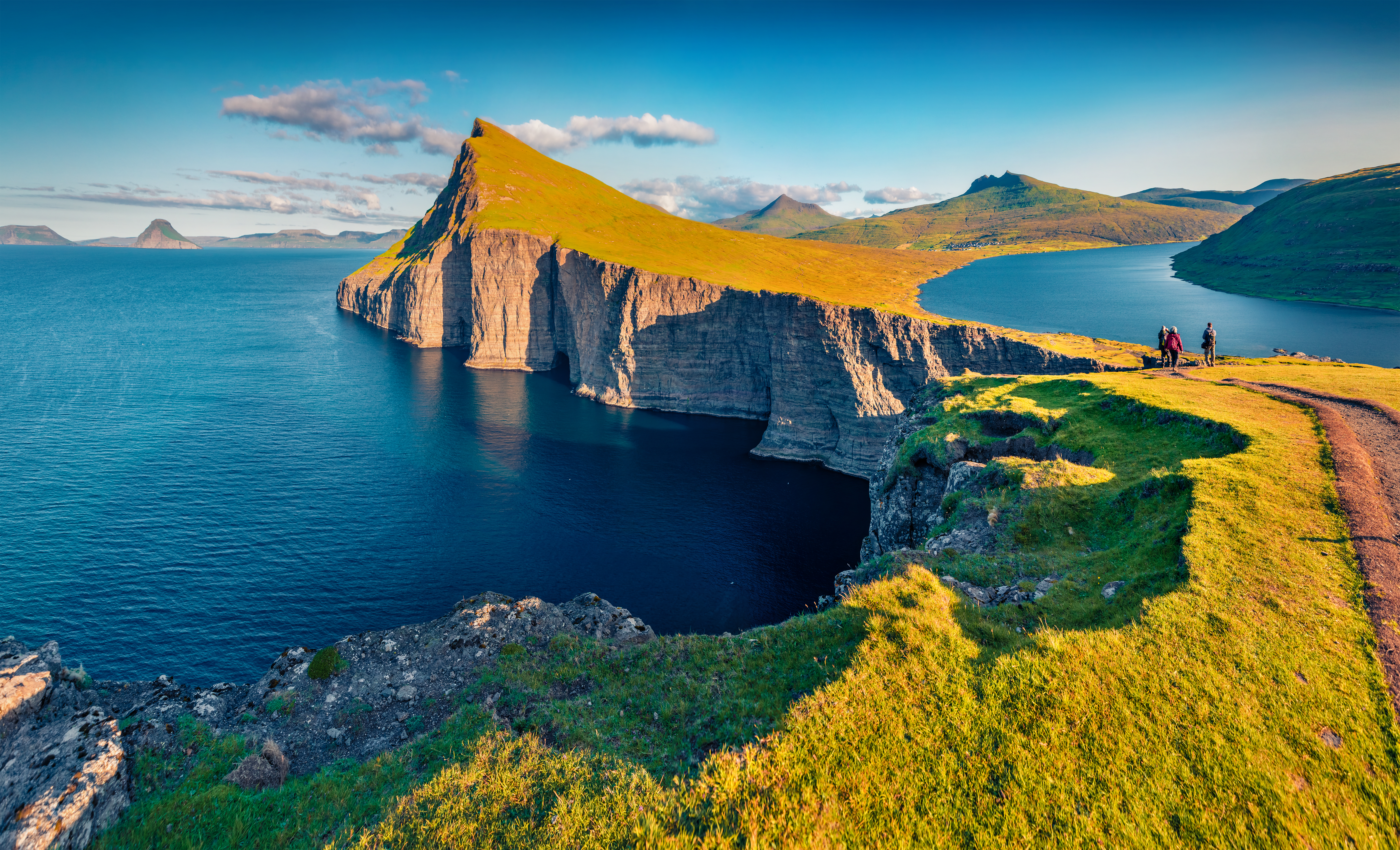 Vandrere ved Sørvágsvatn-søen på Vágar, Færøerne, med fantastisk udsigt over Atlanterhavet, hvor søen synes at svæve over havet