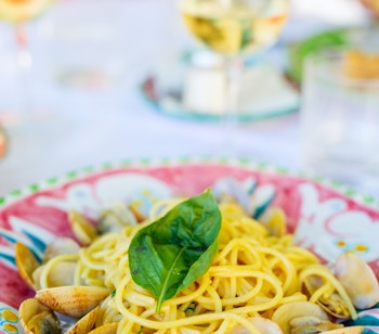 Frisklavet spaghetti med muslinger serveret med hvidvin på en dekorativ tallerken - en lokal specialitet fra Amalfis berømte middelhavskøkken