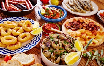 Farverigt udvalg af traditionelle spanske tapas med rejer, blæksprutte, muslinger og oliven serveret med citron på træfade