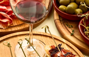 Traditionel spansk tapas-anretning med lufttørret skinke, pølser, oliven og rødvin serveret på et rustikt træbord, en autentisk smagsoplevelse fra Spanien