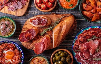 Traditionel spansk tapas anretning med skinke, chorizo, oliven og krydrede kartofler på træbord