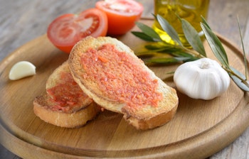 Traditionel spansk Pa amb tomaquet med friskrevet tomat, hvidløg og olivenolie på rustikt træskærebræt