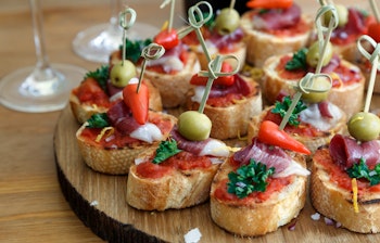 Traditionelle spanske pintxos serveret på rustikt træbræt - små gourmet tapas med brød toppet med farverige ingredienser som oliven, peberfrugt, skinke og friske krydderurter