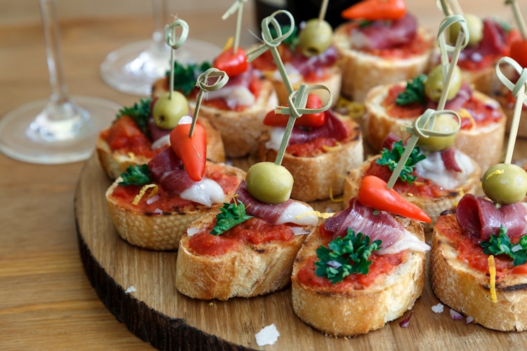 Traditionelle spanske pintxos serveret på rustikt træbræt - små gourmet tapas med brød toppet med farverige ingredienser som oliven, peberfrugt, skinke og friske krydderurter