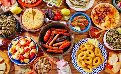 Farverigt udvalg af traditionelle spanske tapas serveret på træbræt med blæksprutte, chorizo, tortilla, oliven og oste - en autentisk smagsoplevelse fra det spanske køkken