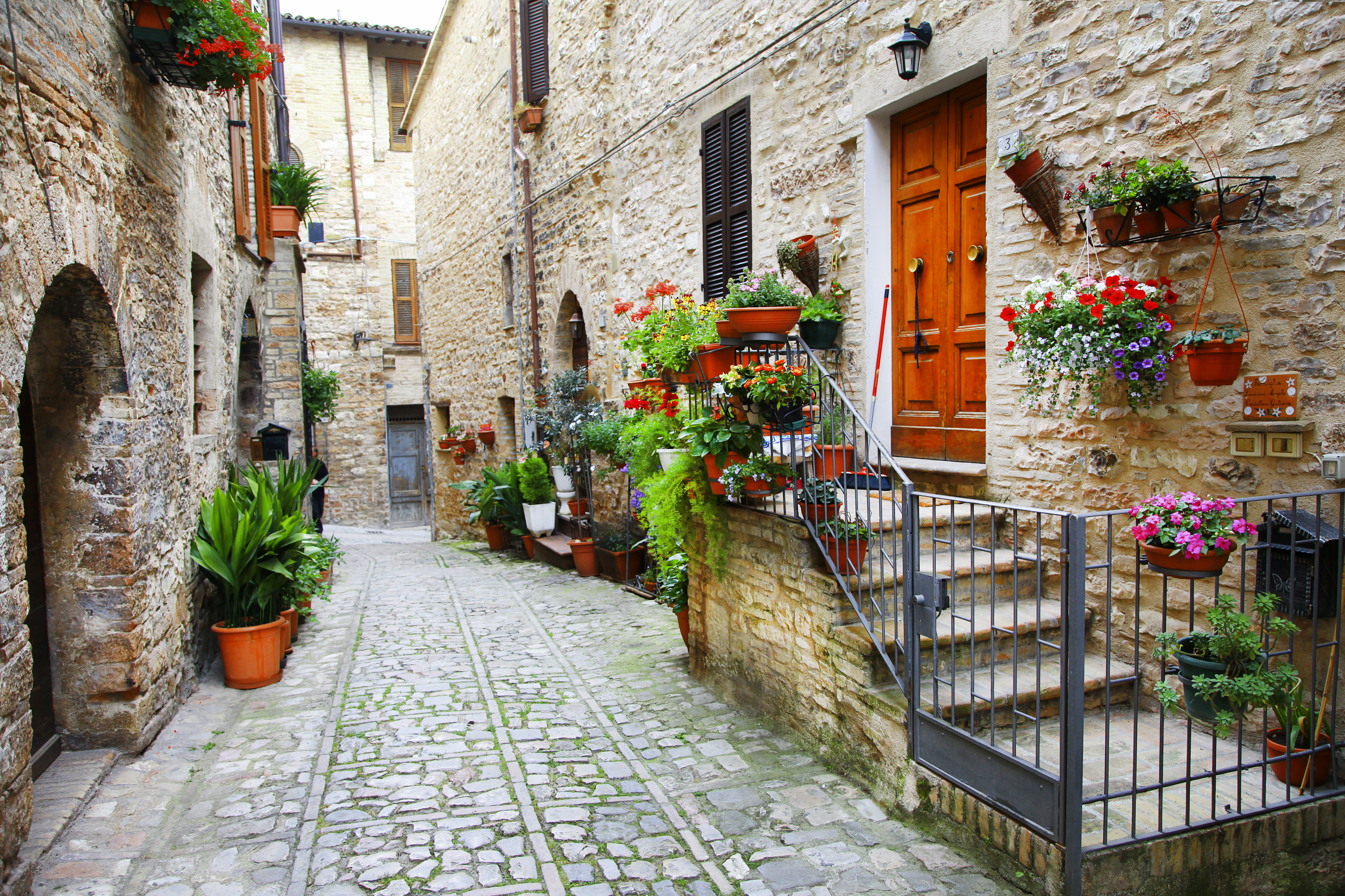 Charmerende middelalderlig stengade med blomsterkrukker i Spello, Umbria