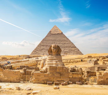 Den store Sphinx i Giza med Khafres pyramide i baggrunden under en klar blå himmel i den egyptiske ørken
