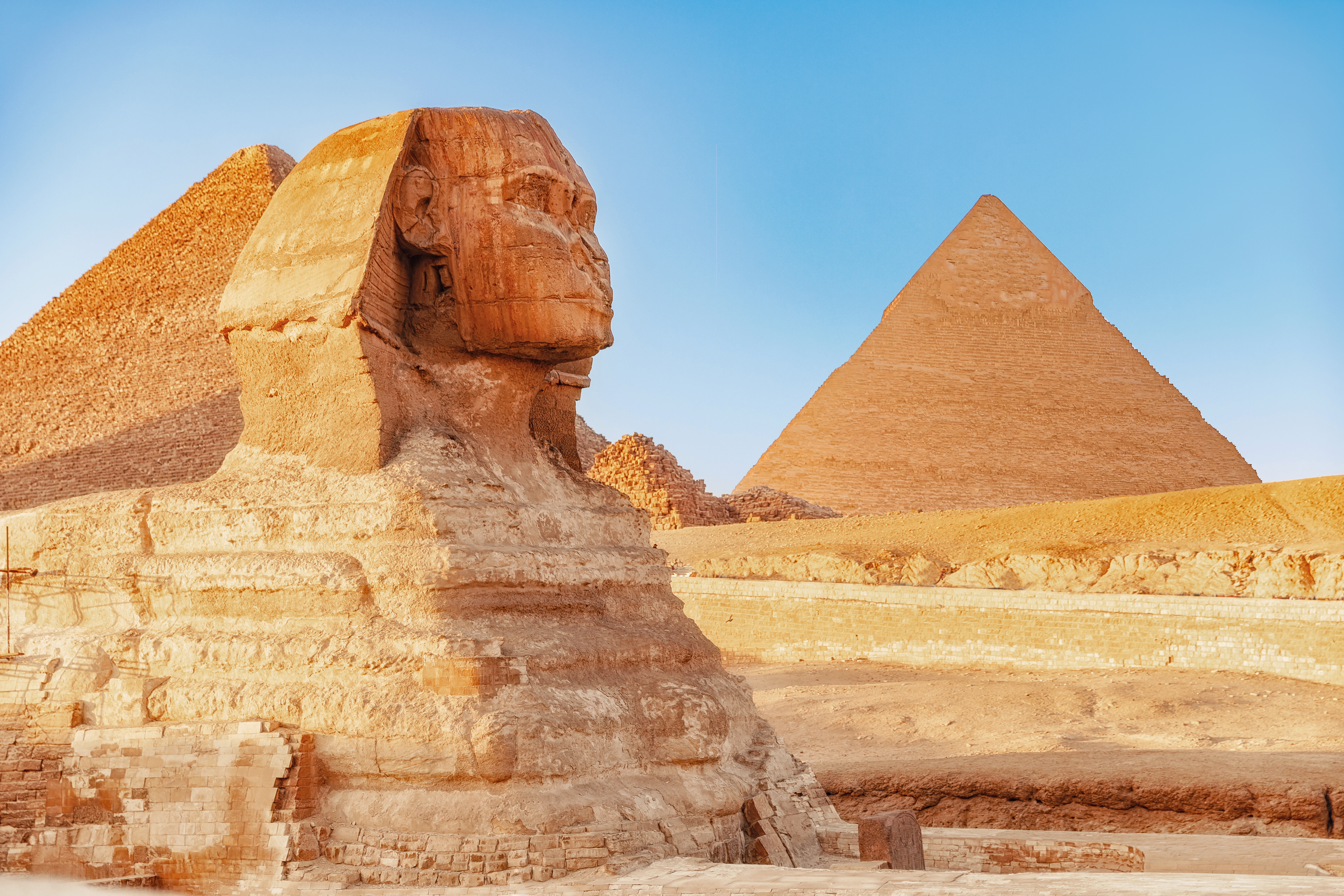 Den store Sphinx i Giza med Khafres pyramide i baggrunden under en klar blå himmel i Egypten