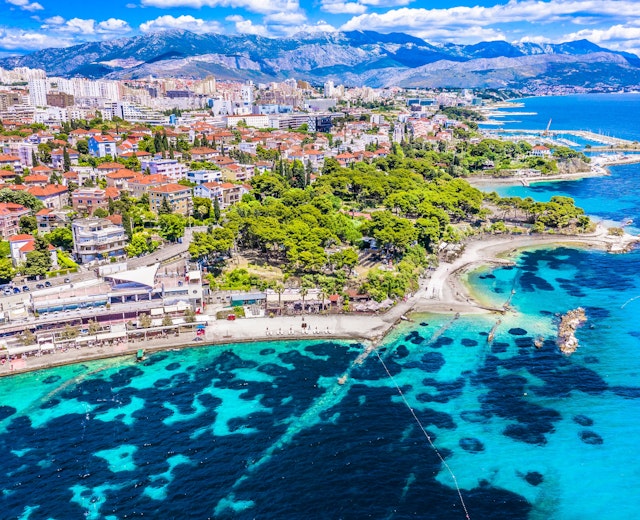 Luftfoto af Split i Kroatien med turkisblåt Adriaterhav, smukke strande og byens arkitektur med bjerge i baggrunden