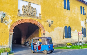 Blå tuk-tuk parkeret foran en livlig gul kolonibygning med buet indgang i Galle Fort, Sri Lanka