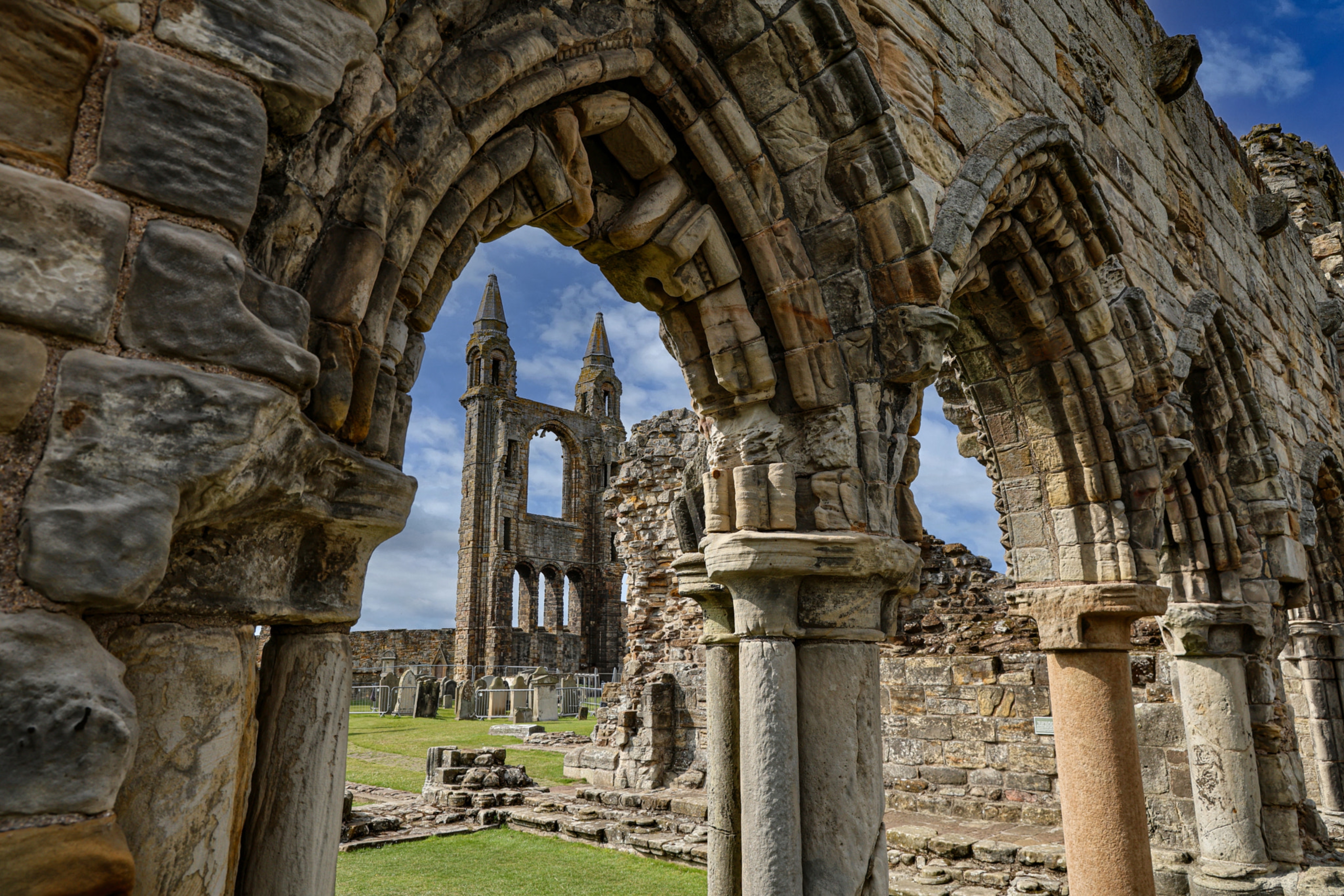 De imponerende ruiner af St Andrews Katedral i Fife, Skotland, med smukke gotiske buer og tvillinge tårne mod en blå himmel