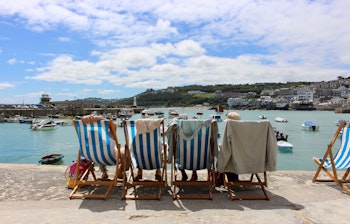 Turister nyder solskinsvejr på den smukke sandstrand i St. Ives, Cornwall med blå himmel og roligt hav