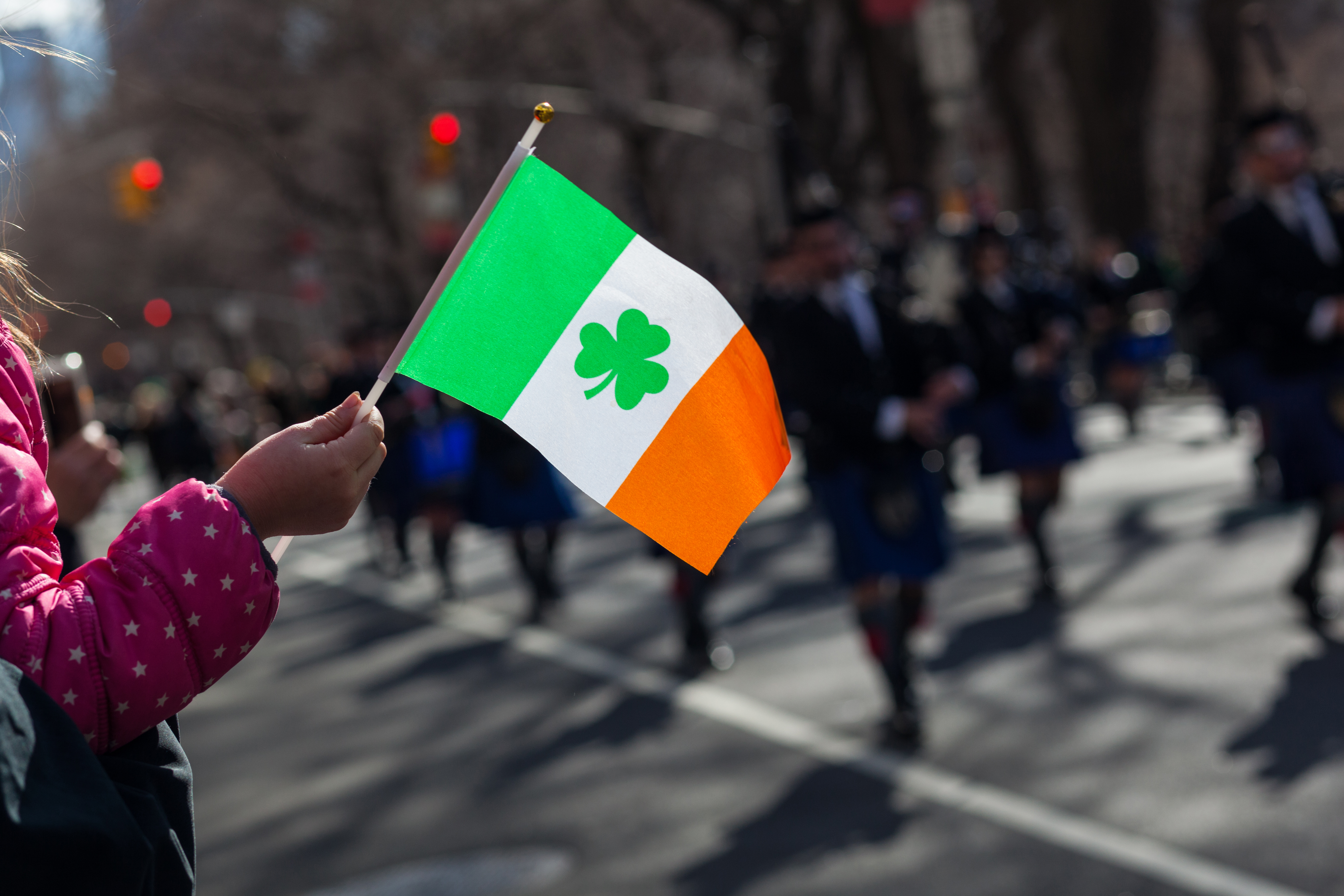 Festlig St. Patrick's Day parade med person der vifter med det irske flag i gaderne omgivet af tilskuere under den traditionelle irske fejring