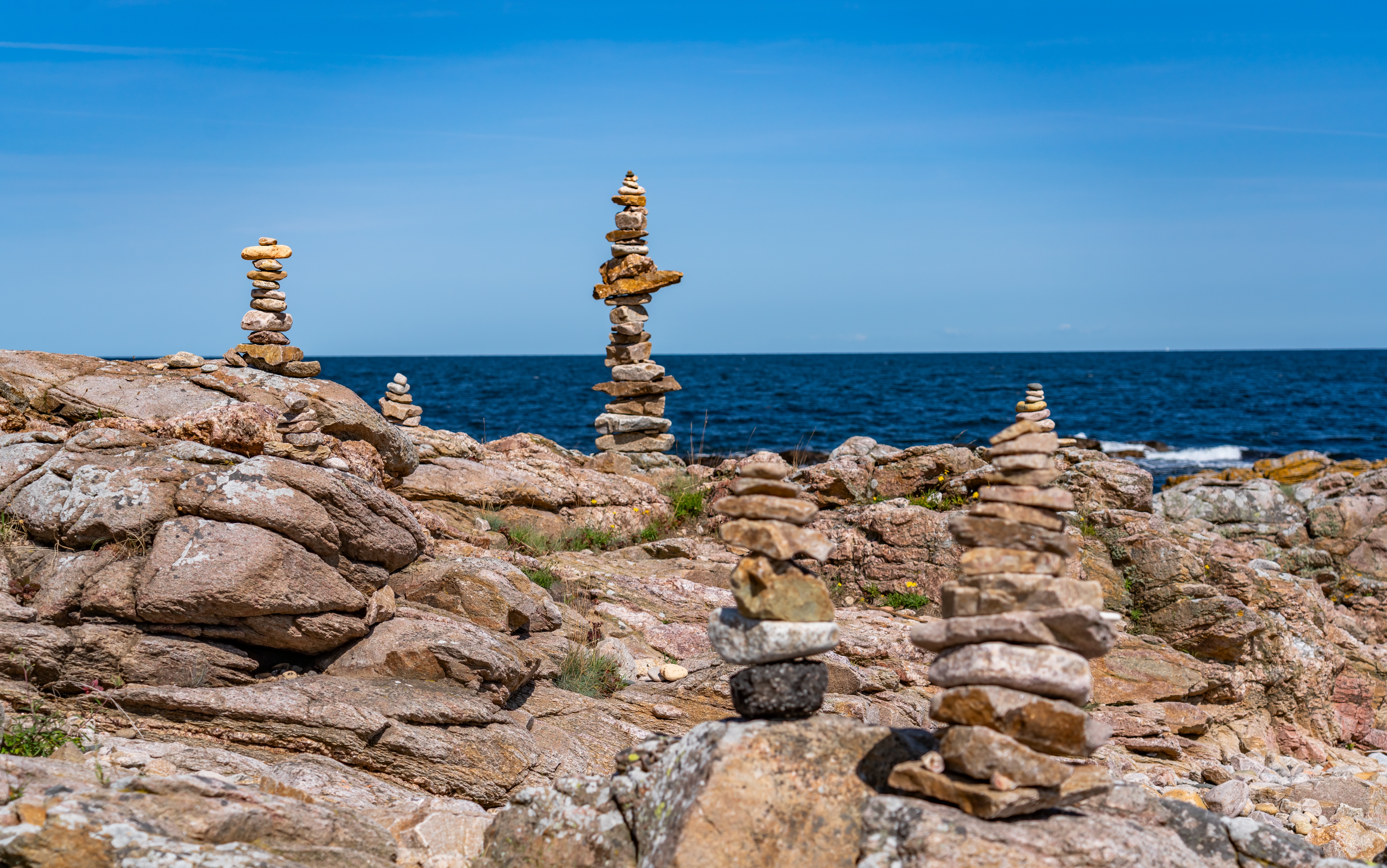 Balancerede stenstakke opstillet på klippekysten i Gudhjem på Bornholm med det blå Østersøen i baggrunden