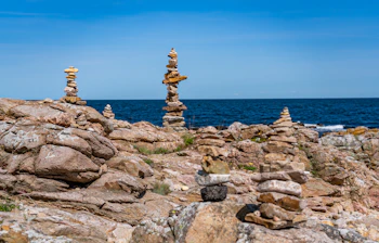 Balancerede stenstakke opstillet på klippekysten i Gudhjem på Bornholm med det blå Østersøen i baggrunden