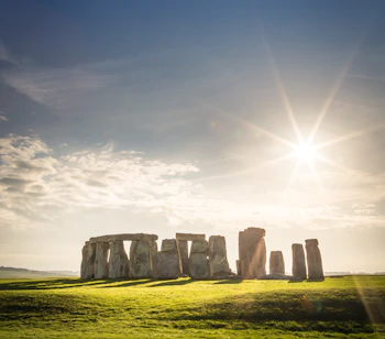 Det berømte Stonehenge stenmonment i England med solstråler og grønt landskab