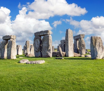 Det berømte stenmonument Stonehenge i England med sin karakteristiske cirkelformation af megalitter på en grøn græsmark under en klar blå himmel - et mystisk UNESCO-verdensarvssted fra forhistorisk tid.