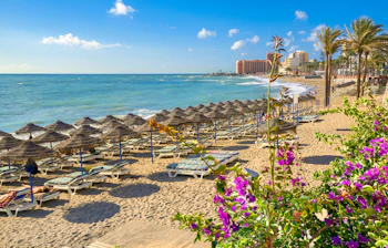 Indbydende sandstrand med farverige parasoller og svajende palmer i ferieresorten Benalmadena ved det azurblå Middelhav på Costa del Sol i Spanien