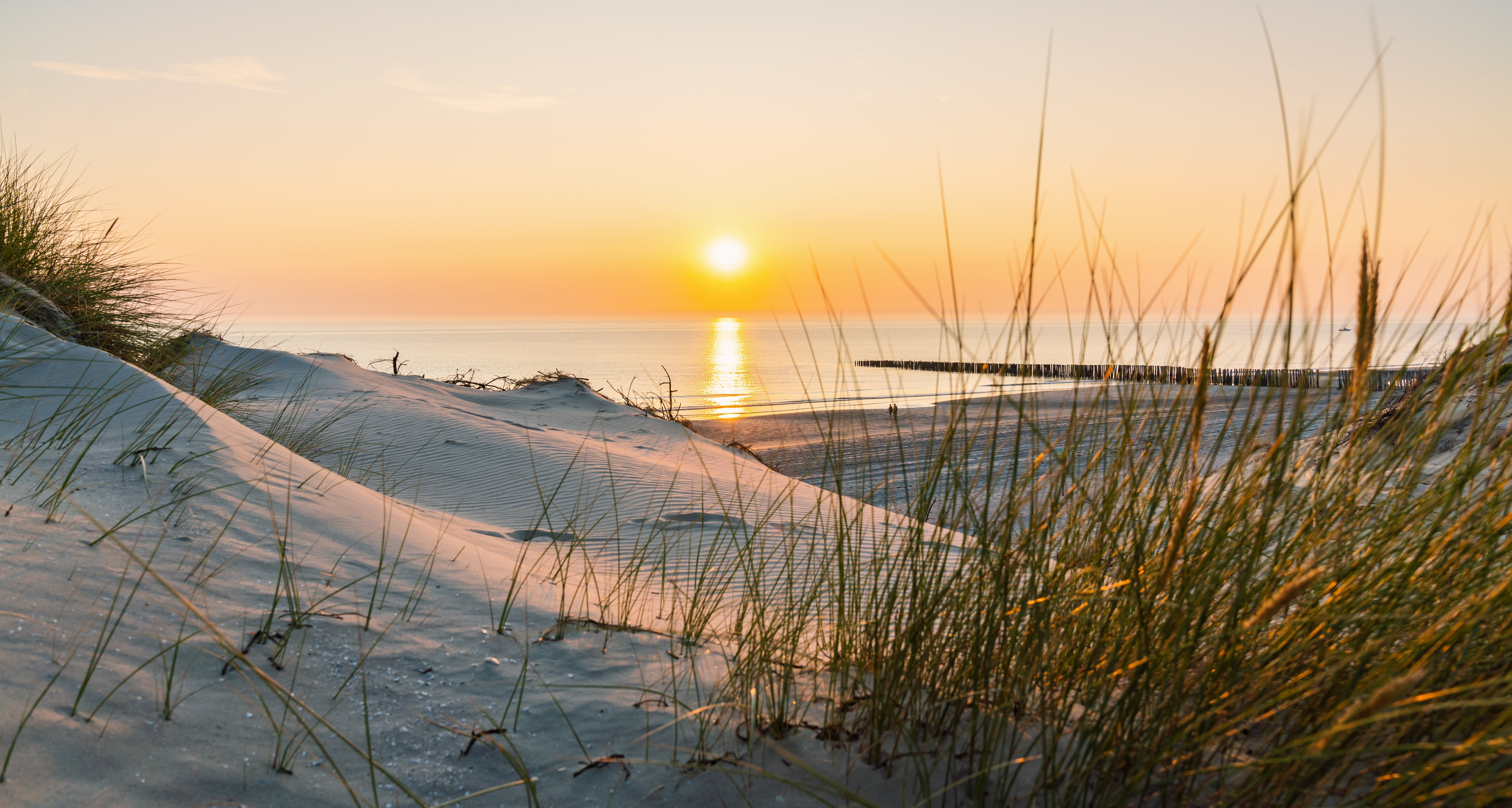 Smuk solnedgang over klitter og strand ved Vestjyllands kyst med træmole i baggrunden