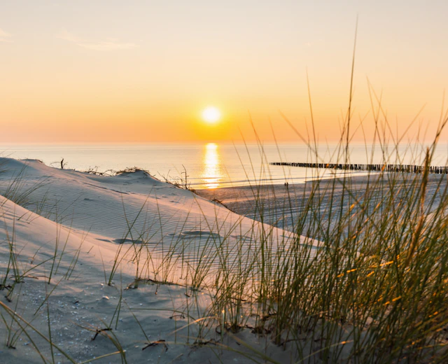 Smuk solnedgang over klitter og strand ved Vestjyllands kyst med træmole i baggrunden