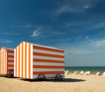 Farverige rød-hvide og blå-hvide stribede strandkabiner på den solrige sandstrand i De Panne ved den belgiske Nordsøkyst