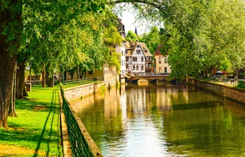 Idyllisk kanalparti i Petite France-kvarteret i Strasbourg med charmerende bindingsværkshuse og træer ved bredden, UNESCO-verdensarv i Alsace, Frankrig