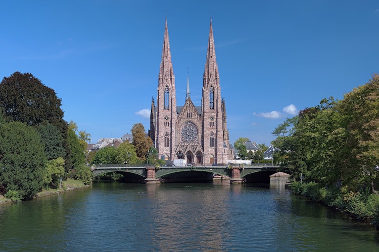 Den historiske Saint-Paul kirke med sine gotiske tårne spejler sig i Ill-floden i Strasbourg, et smukt eksempel på Alsace-regionens arkitektur