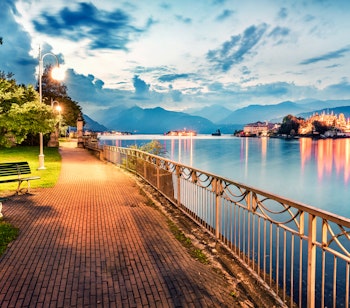 Stemningsfuld aftenudsigt over Stresa med den oplyste strandpromenade langs Lago Maggiore ved solnedgang, og den berømte Isola Bella ø i baggrunden
