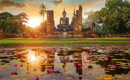 Gammel Buddha statue ved Sukhothai Historiske Park i Thailand med lotus blomster og solnedgang