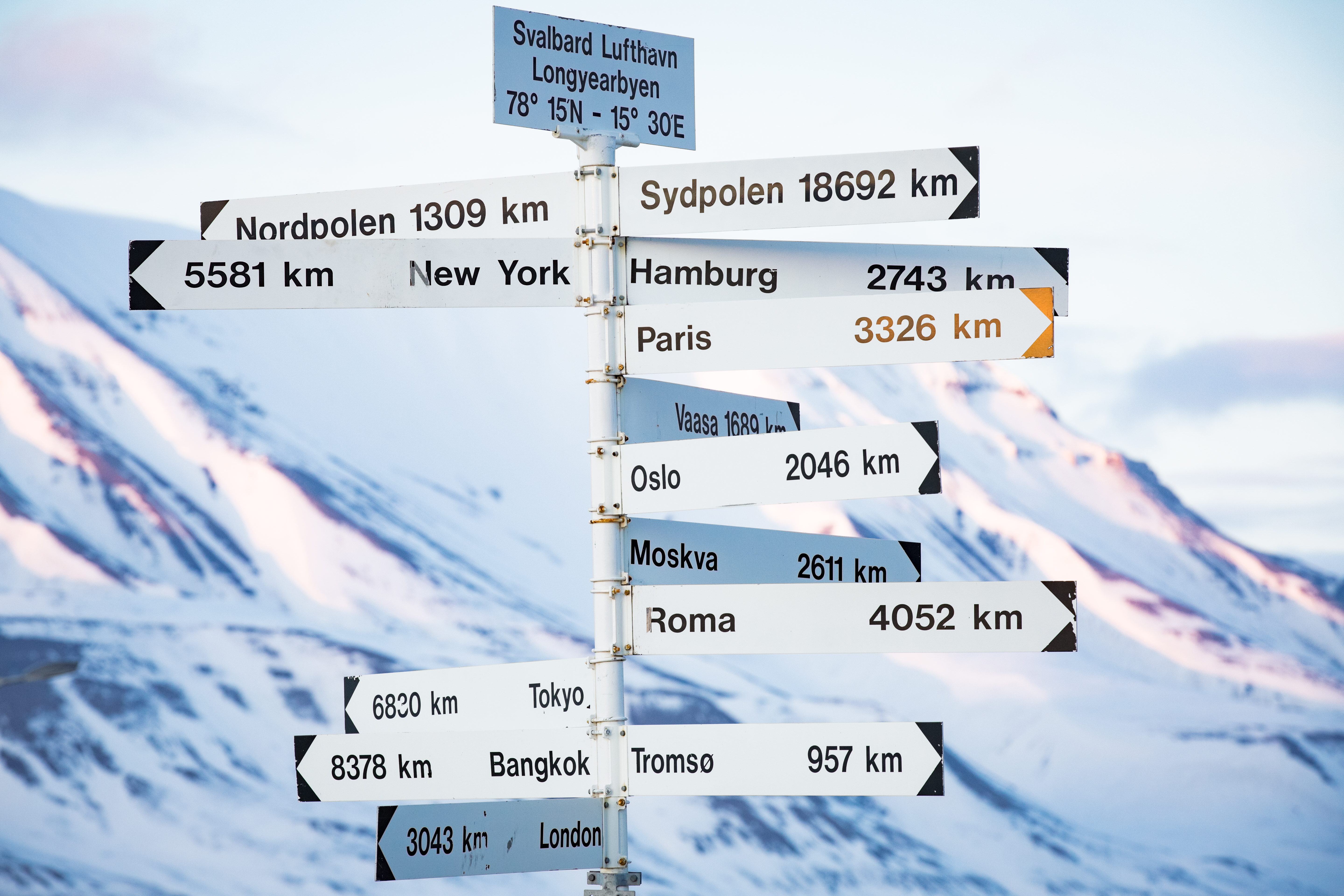 Destinationsskilt på Svalbard Longyearbyen der viser afstande til verdenshovedstæder med snedækkede arktiske bjerge