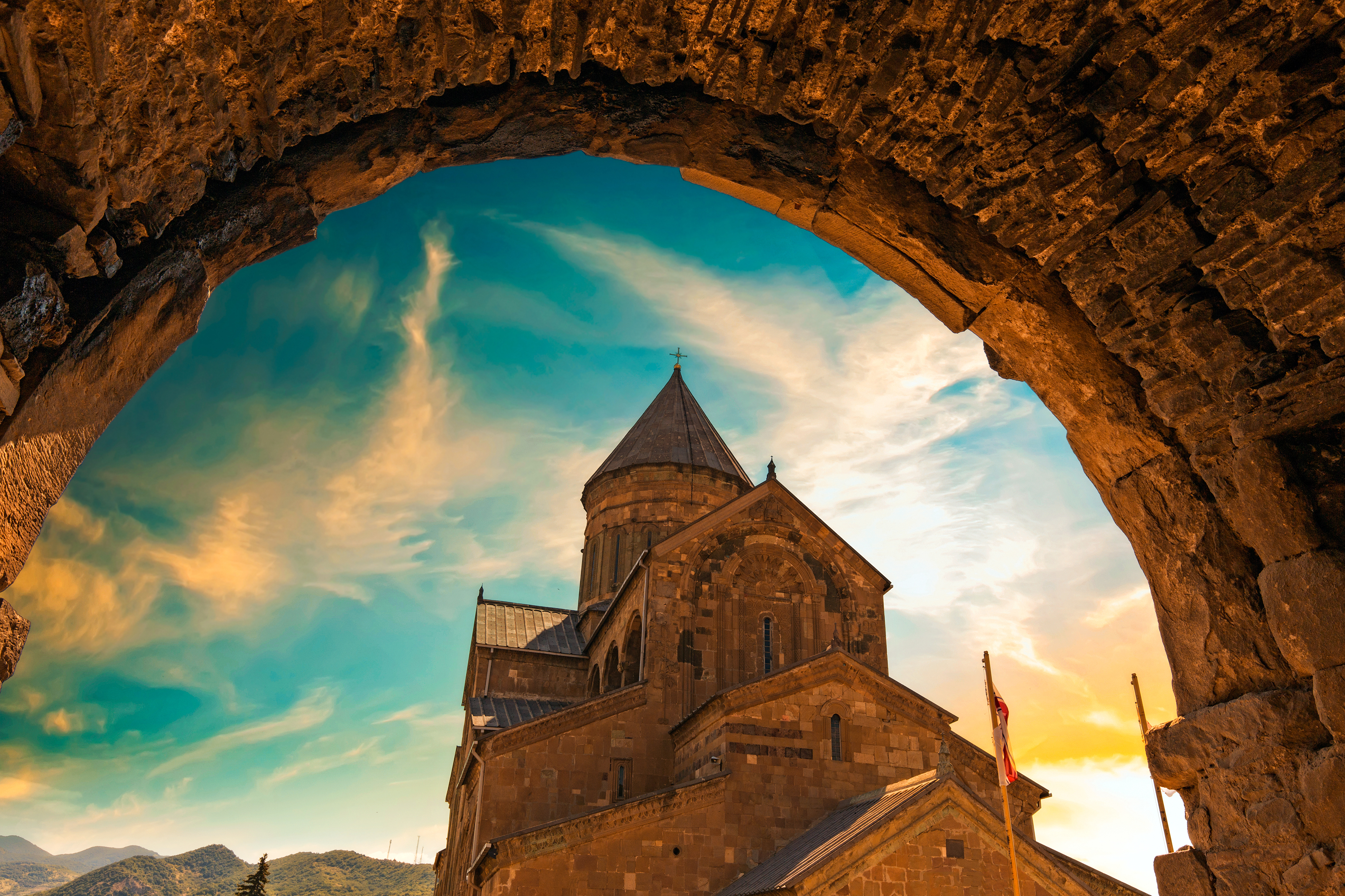 Historisk Svetitskhoveli-katedral i Mtskheta, Georgien, set gennem en gammel stenbue ved solnedgang med dramatisk himmel