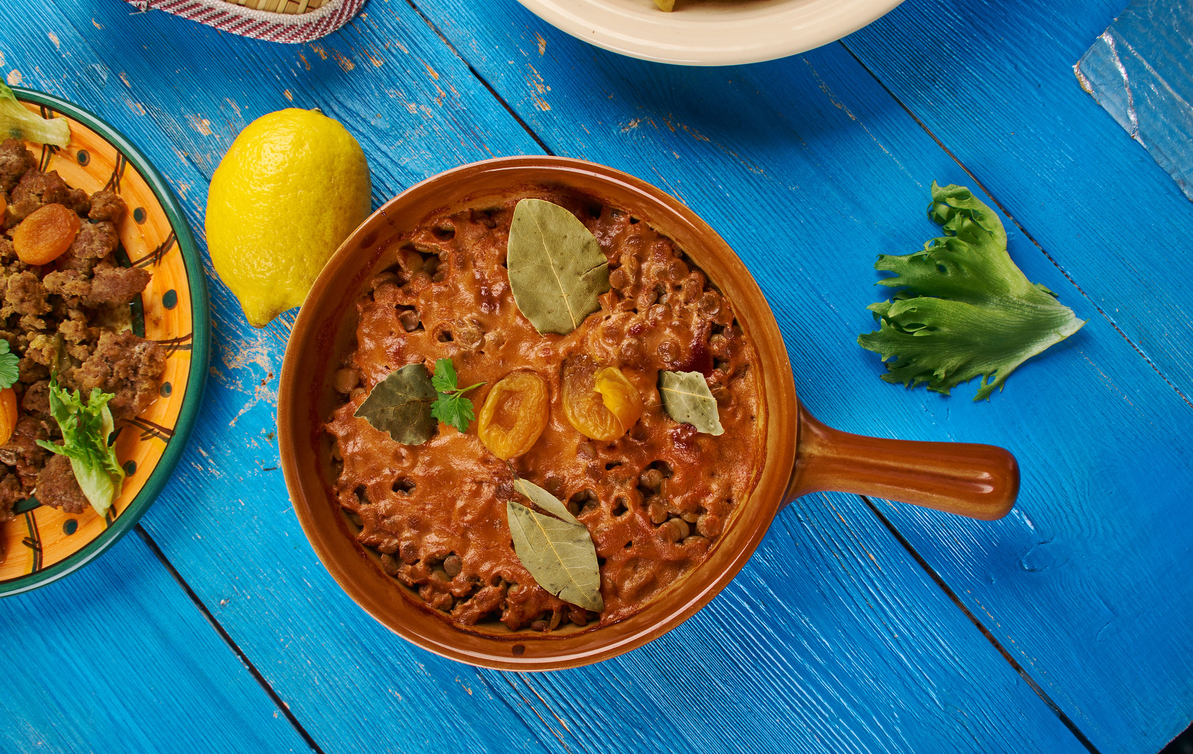 Traditionel feijoada med sorte bønner serveret i lerkar på blåt træbord med citron