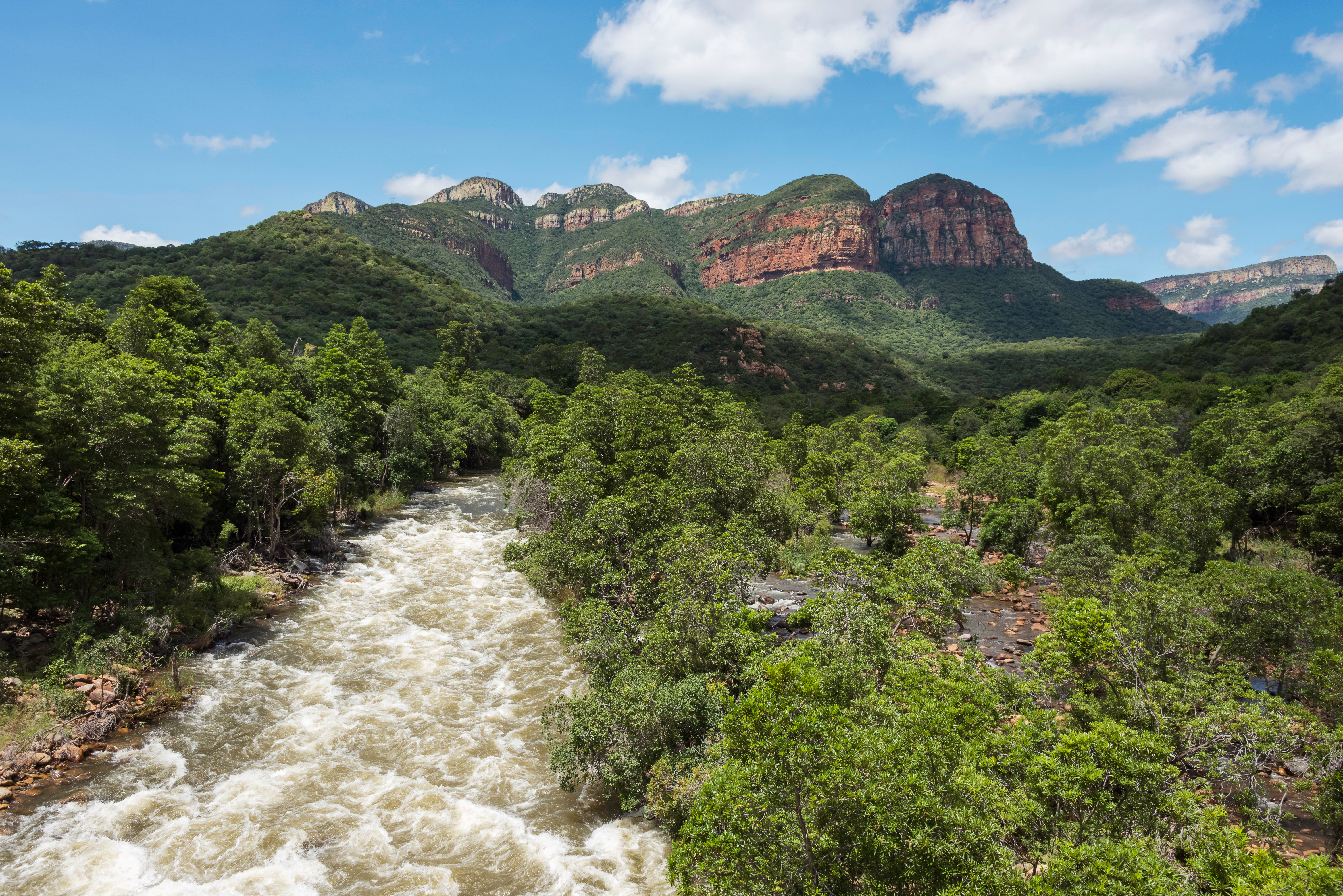 Dramatisk flodlandskab i Sydafrika med grønne bjerge og røde klipper under blå himmel