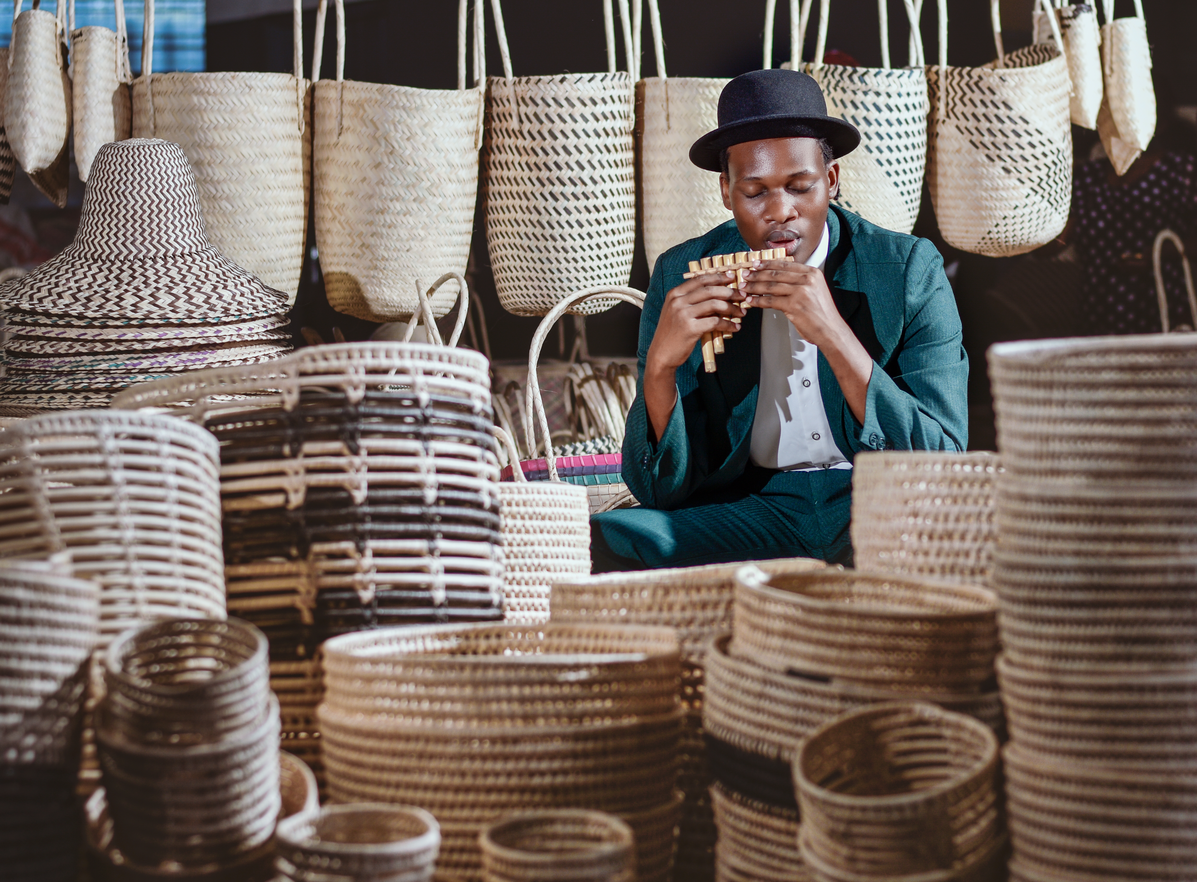 Lokal håndværker spiller på panfløjte blandt traditionelle stråkurve og tasker på marked i Durban, Sydafrika