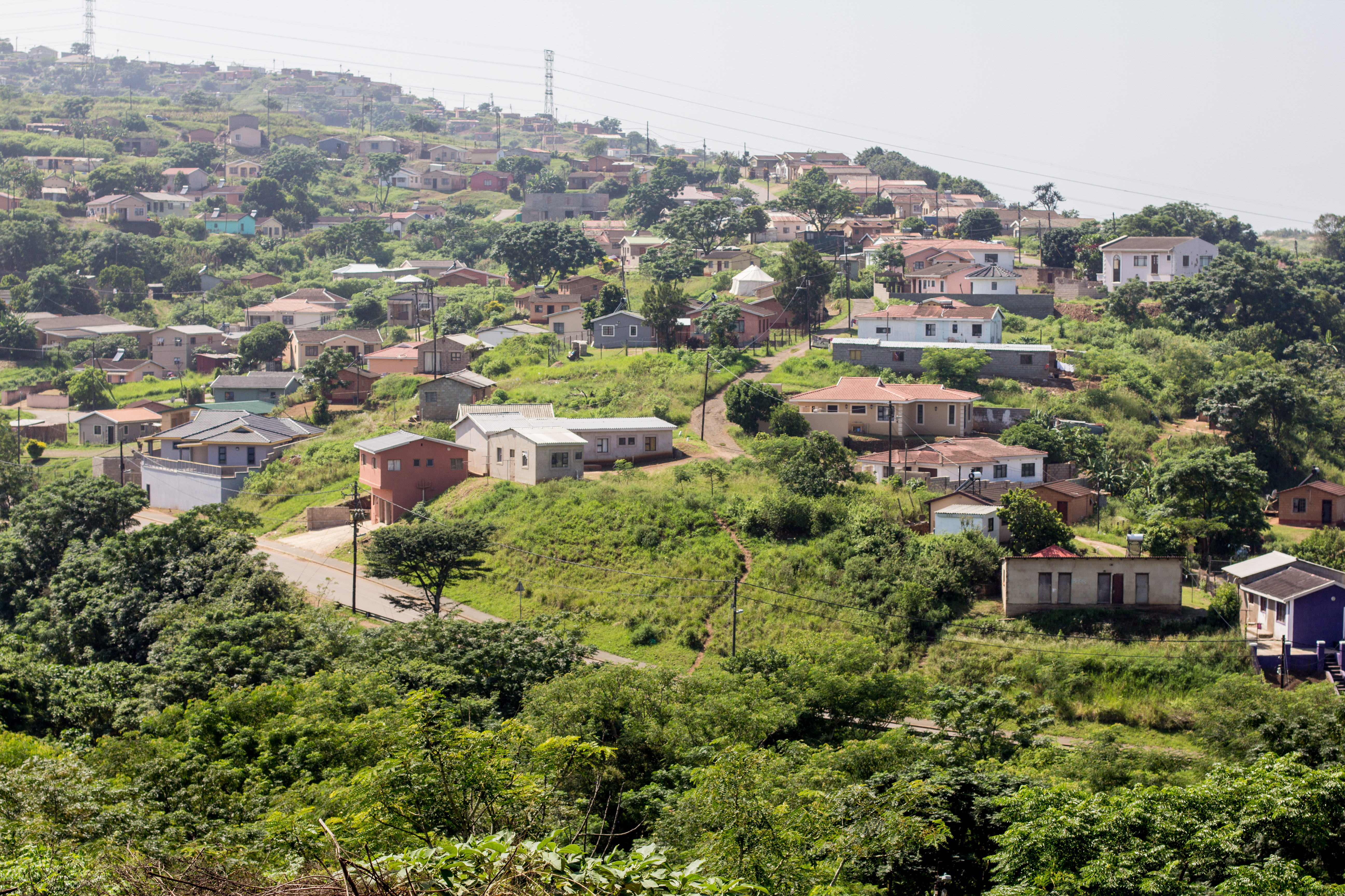 Sydafrikansk bydel med farverige huse spredt på grønne bakker mellem frodig vegetation