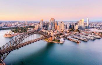 Sydney Harbour Bridge og Opera House ved solnedgang med byens skyline