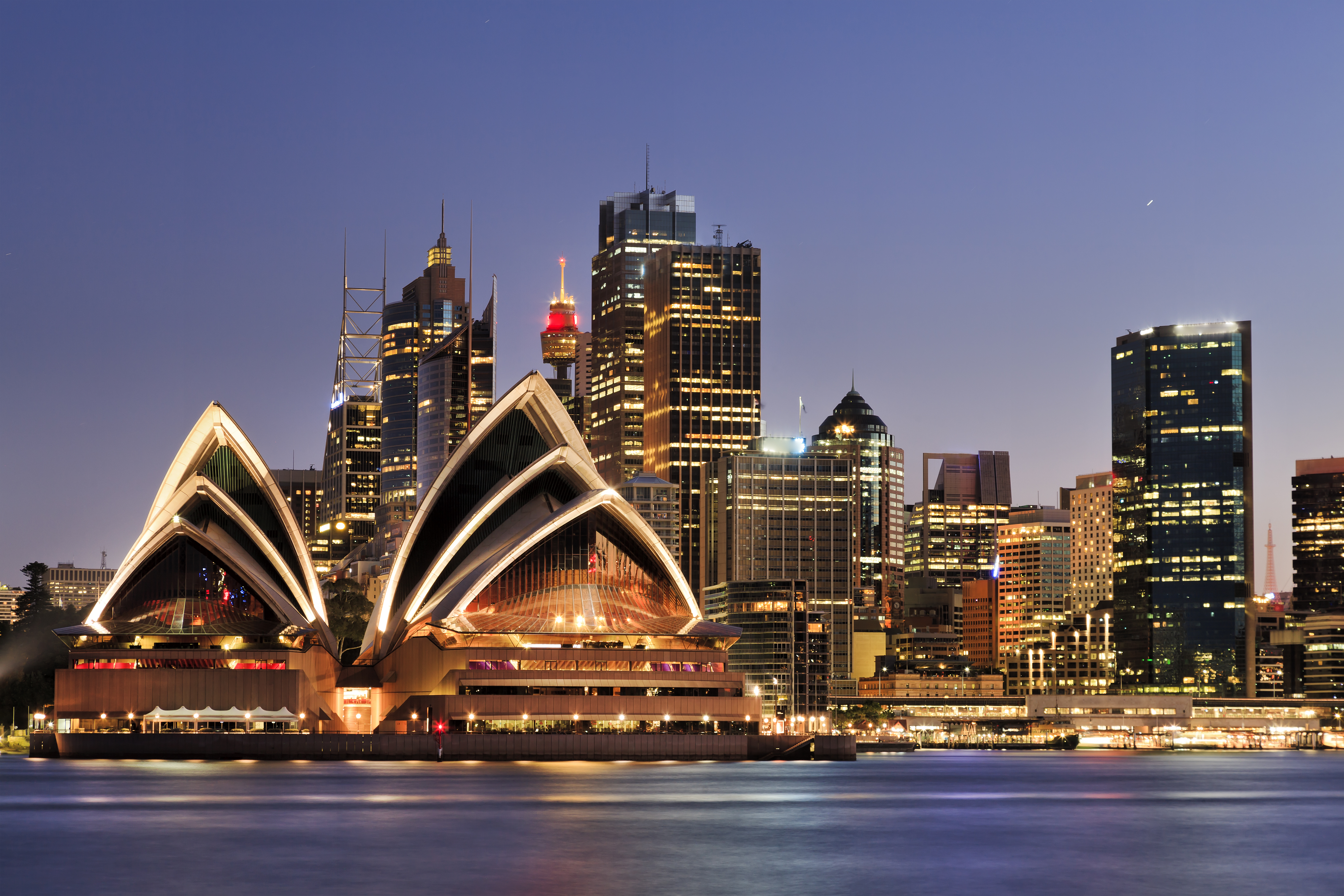 Sydney Opera House oplyst i aftenlys med byens skyline og refleksioner i havnen set fra Cremorne Point, Australien