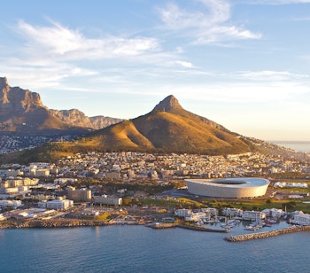 Betagende luftfoto af Table Mountain i Cape Town under den gyldne time, med Lions Head og Atlanterhavet i baggrunden, perfekt til en eventyrlig ferie i Sydafrika