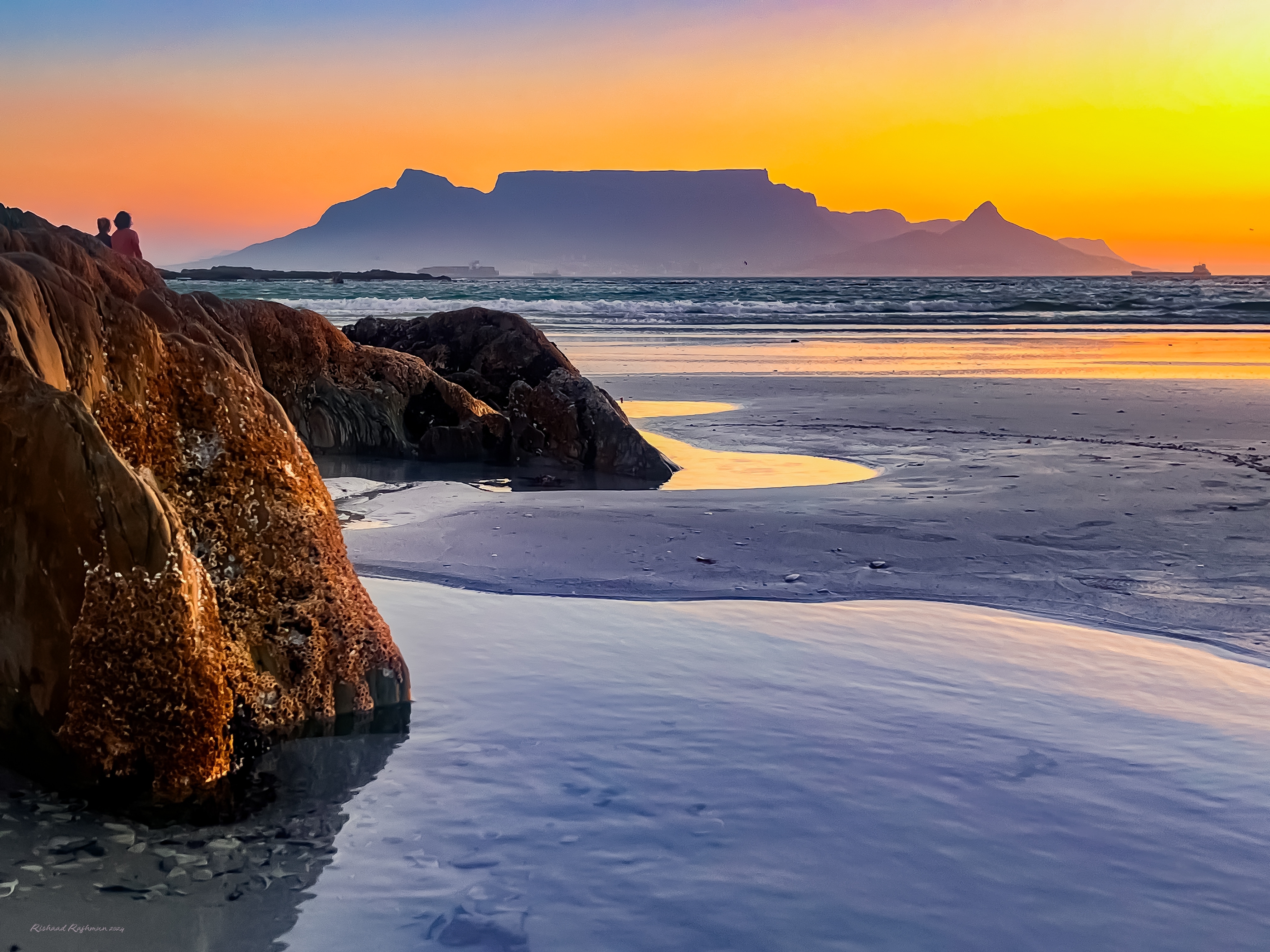 Table Mountain i solnedgang set fra klippefyldt strand i Kapstaden Sydafrika