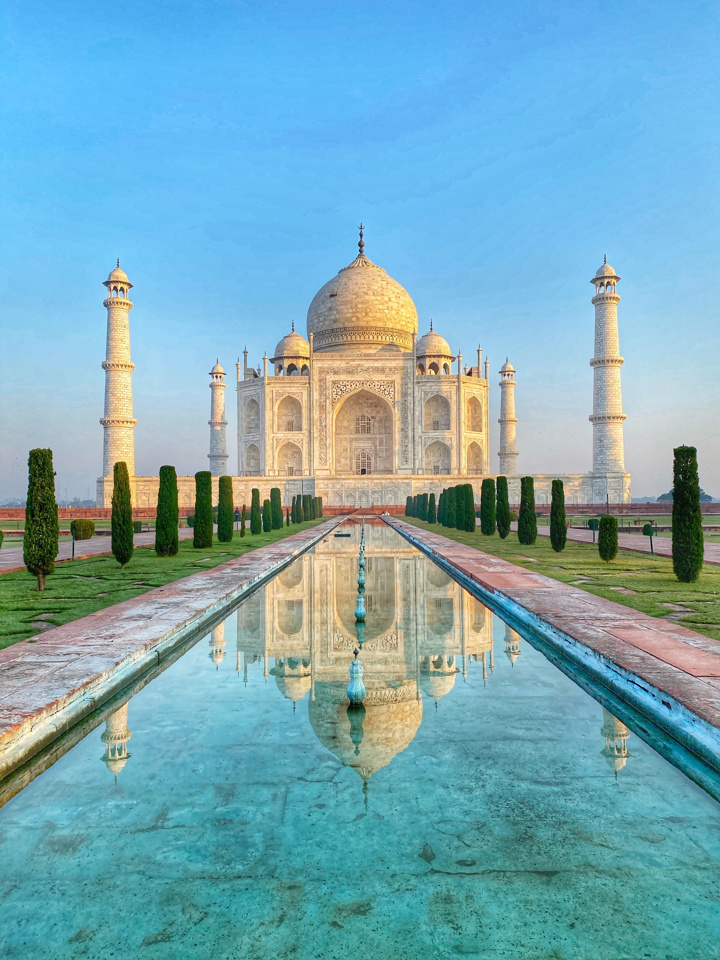 Taj Mahal ved solopgang i Agra, Indien, med perfekt spejling i vandkanalen og blå himmel