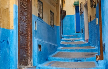 Charmerende blåmalet smal gyde med traditionel trædør i den historiske medina i Tanger, der viser den karakteristiske arkitektur og de smukke farver i Nordmarokko