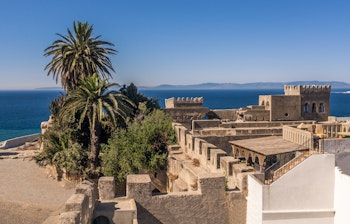 Panoramaudsigt over den historiske medina i Tanger med hvide bygninger og fæstningsmure, der skuer ud over Gibraltarstrædet mod den spanske kyst