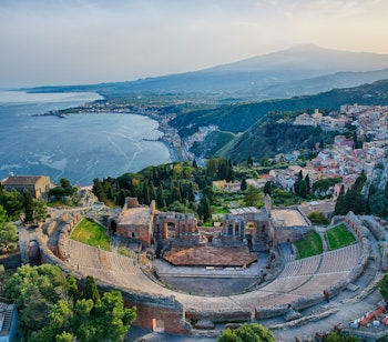 Luftfoto af det historiske græsk-romerske amfiteater i Taormina på Sicilien med betagende udsigt over Middelhavet og Etna-bjerget