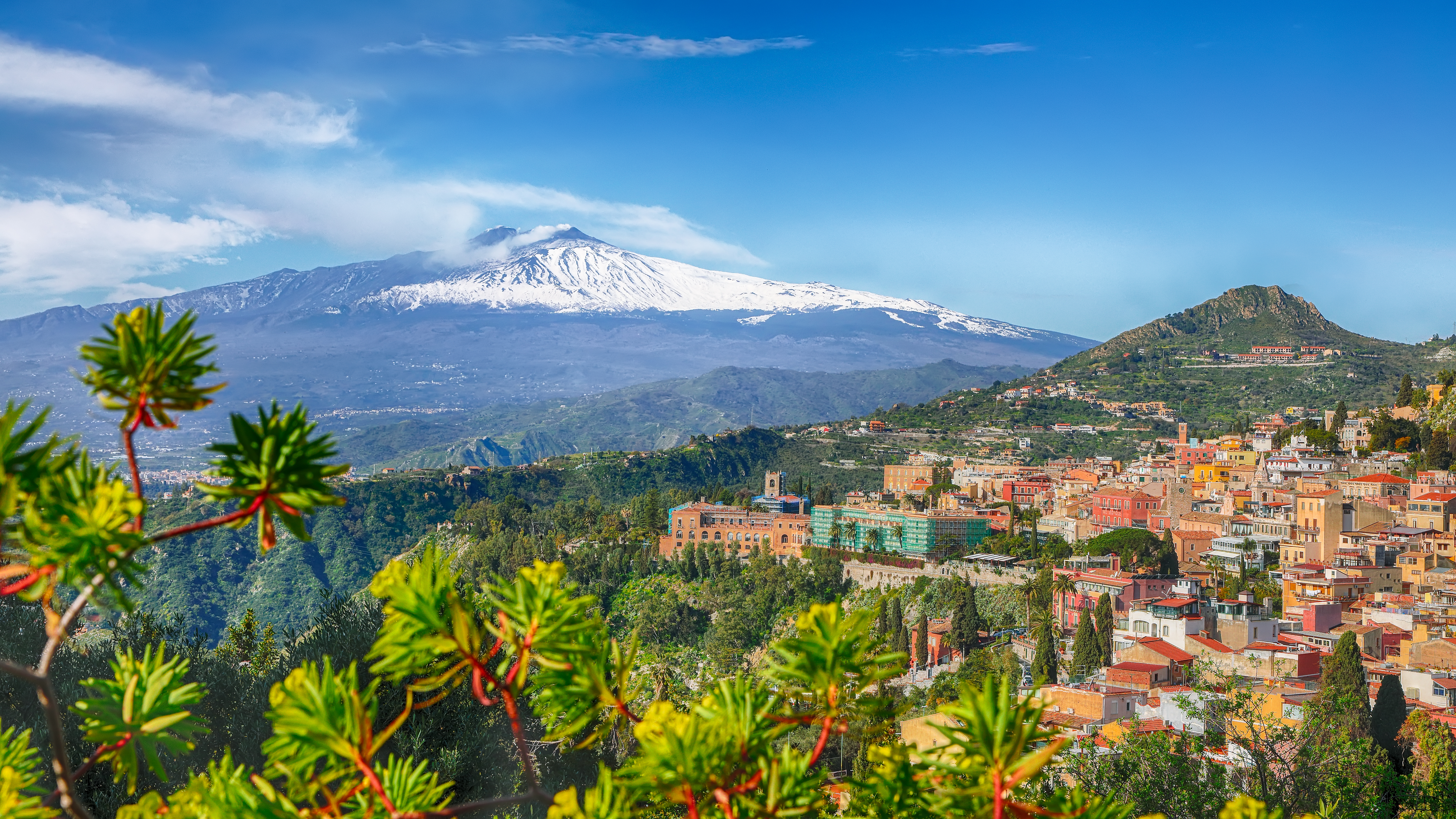 Betagende luftpanorama over Taormina by med dens karakteristiske røde tage og den rygende snedækkede Etna-vulkan i baggrunden, en ikonisk udsigt på Sicilien i Italien