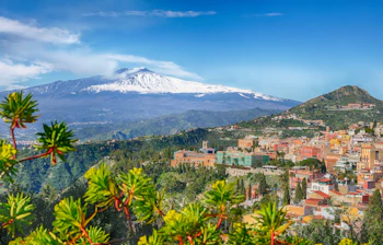 Betagende luftpanorama over Taormina by med dens karakteristiske røde tage og den rygende snedækkede Etna-vulkan i baggrunden, en ikonisk udsigt på Sicilien i Italien